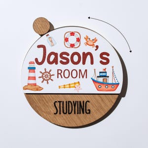 May include: A round wooden sign with a nautical theme. The top half is white with the text "Jason's ROOM" in red, and nautical illustrations. The bottom half is wood-grain with the word "STUDYING". A small wooden knob is attached at the top.