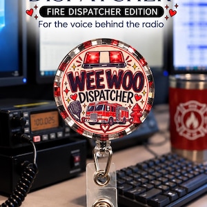 May include: A circular badge reel featuring a red fire engine, a fire hydrant, and a radio microphone graphic. The text reads WEE WOO DISPATCHER. The border is red and white with a glittery finish. A clear plastic strap with a metal snap is attached.