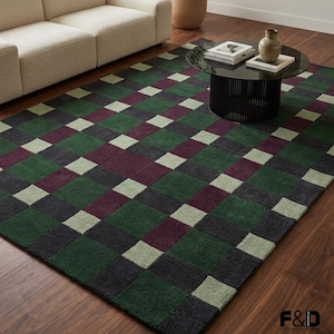 Puede incluir: Una alfombra rectangular con un diseño geométrico de tablero de ajedrez. La alfombra presenta cuadrados de color verde oscuro, verde claro, burdeos y gris carbón. Está colocada sobre un suelo de madera, con un sofá y una mesa de centro al fondo.