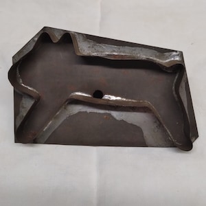 May include: A vintage metal cookie cutter shaped like a running horse. The cutter is made of dark metal with a worn, rustic appearance. It has a small hole in the center.