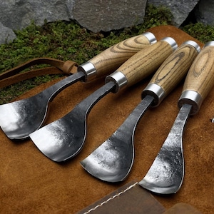 May include: Set of four wood carving tools with curved blades and wooden handles. The tools are laid out on a brown leather surface.