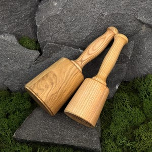 May include: Two wooden mallets with cylindrical heads and long, smooth handles. The mallets are crafted from light-colored wood with a visible grain pattern. The tools feature a solid construction with rounded ends on the handles and flat faces.