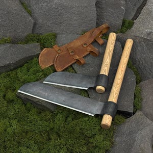 Könnte beinhalten: Zwei Handwerkzeuge mit dunkelgrauen Metallklingen und hellen Holzgriffen, begleitet von einer braunen Lederscheide mit Metallnieten und Riemen. Die Werkzeuge haben gebogene, scharfkantige Klingen, die an zylindrischen Holzgriffen befestigt sind.