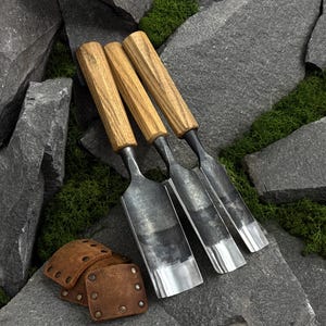 May include: Three hand tools with polished metal blades and light brown wooden handles, arranged side by side. Next to the tools are several small, square, brown leather patches, each featuring four metal rivets at the corners.