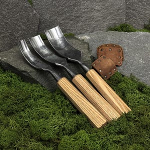 Puede incluir: Tres gubias para tallar madera con hojas metálicas curvas y mangos de madera clara. Las herramientas cuentan con cabezas de acero pulido de diferentes anchos y vienen acompañadas de dos pequeños protectores de hoja cuadrados de cuero marrón.