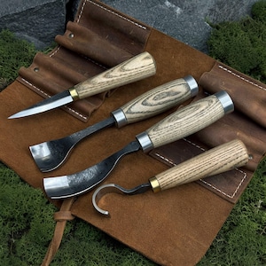 May include: A set of four wood carving tools with ash wood handles and metal blades, displayed on a brown leather tool roll. The tools include a knife, two gouges, and a hook knife, ideal for woodworking projects.