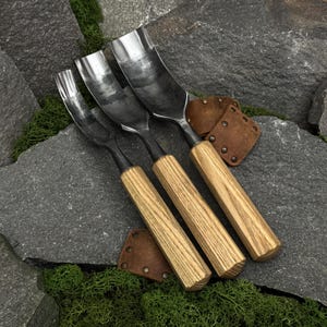May include: A set of three wood carving gouges with curved metal blades and light-colored wooden handles. The tools feature polished steel heads with varying widths and are accompanied by two small, brown leather protective covers with metal rivets.