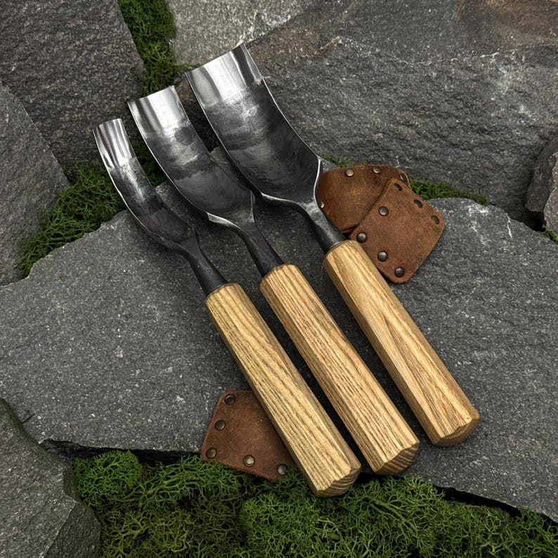 May include: A set of three wood carving gouges with curved metal blades and light-colored wooden handles. The tools feature polished steel heads with varying widths and are accompanied by two small, brown leather protective covers with metal rivets.