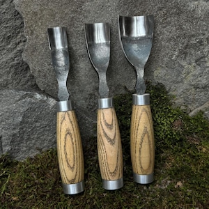 May include: Three wood carving tools with metal blades and wooden handles. The handles are a light brown with dark brown wood grain.