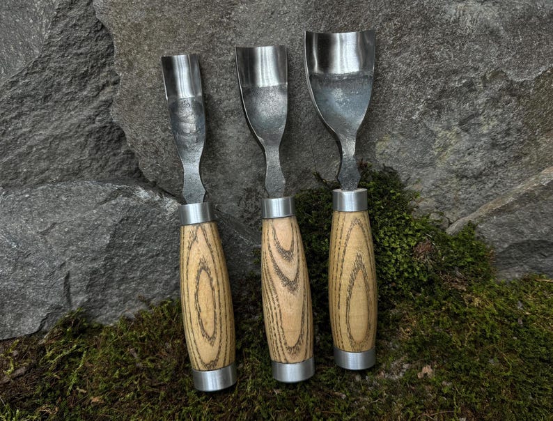 May include: Three wood carving tools with metal blades and wooden handles. The handles are a light brown with dark brown wood grain.