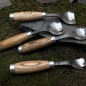 May include: Four wood-handled carving tools with metal blades. The tools have different shapes and sizes. The handles are made of light brown wood with dark brown streaks.
