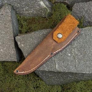 Knife removed from leather sheath showing wooden handle and blade, carving knife and leather knife case set