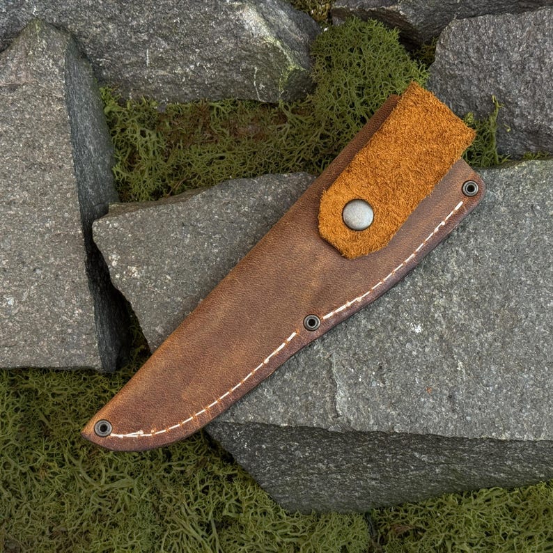 Knife removed from leather sheath showing wooden handle and blade, carving knife and leather knife case set