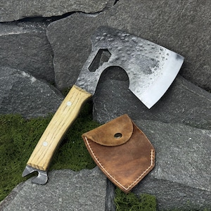 Peut inclure: Une petite hache forgée à la main avec un manche en bois et un ouvre-bouteille. La tête de la hache a une finition sombre texturée et une lame tranchante. Un étui en cuir marron avec des coutures blanches protège la lame.