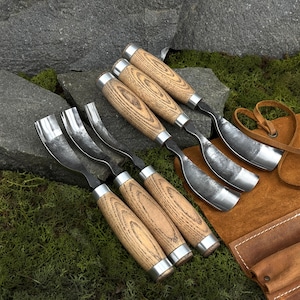 May include: A set of five wood carving gouges with curved metal blades and light brown wooden handles. Each tool features a cylindrical handle with a visible wood grain pattern and a silver metal ferrule connecting the handle to the steel blade.