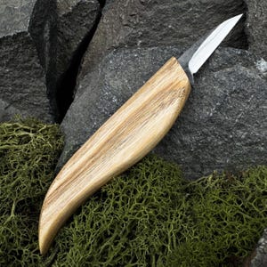 May include: A fixed-blade knife featuring a sharp, pointed steel blade and a smooth, light-colored wooden handle with visible grain patterns. The handle has a curved, ergonomic shape that tapers toward the base, providing a secure grip.
