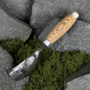 May include: A wood carving gouge featuring a curved, polished steel blade and a cylindrical wooden handle with a visible grain pattern. The tool includes two silver-colored metal ferrules at the top and bottom of the handle for reinforcement.