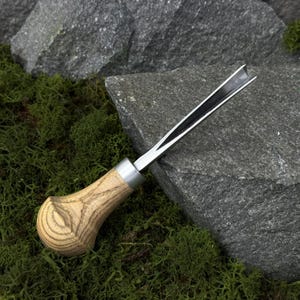 May include: A wood carving gouge with a curved blade. The handle is made of light-colored wood with a textured grain pattern. The metal blade is silver and black, and the tool is designed for detailed woodworking.