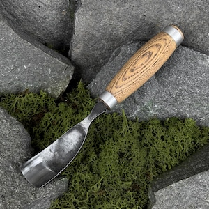 May include: A wood carving gouge featuring a curved, polished metal blade and a cylindrical wooden handle with a visible grain pattern. The handle is secured with a silver-toned metal ferrule at the top and a matching metal cap at the base.