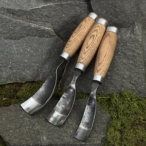 May include: Three hook knives with curved, dark metal blades and light brown wooden handles featuring visible grain patterns. Each tool has a silver-colored metal ferrule connecting the handle to the forged steel blade, designed for woodworking.