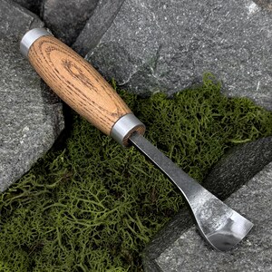 May include: A wood carving tool featuring a smooth, light brown wooden handle with visible grain patterns, secured by two silver-toned metal ferrules at each end, and a curved, polished steel blade designed for scooping or shaping wood.