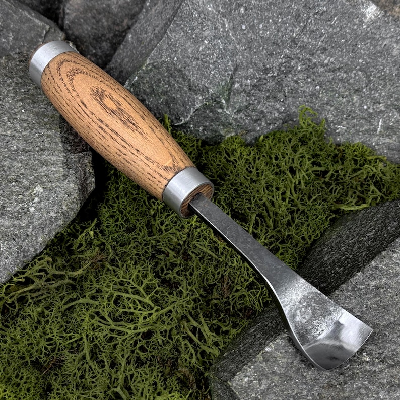 May include: A wood carving tool featuring a smooth, light brown wooden handle with visible grain patterns, secured by two silver-toned metal ferrules at each end, and a curved, polished steel blade designed for scooping or shaping wood.