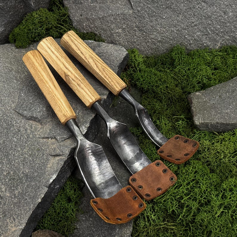 May include: Three hand tools with light brown wooden handles and dark forged metal blades. Each blade features a curved shape and is protected at the tip by a brown leather cover secured with small metal rivets, creating a functional set.