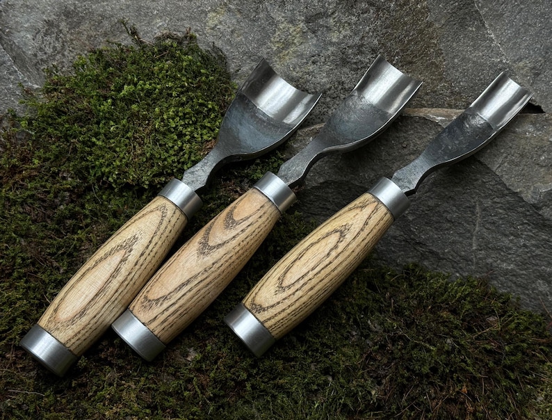 May include: Three wood-handled carving tools with metal blades. The blades are curved and have a rounded tip. The handles are made of light brown wood with a grain pattern.