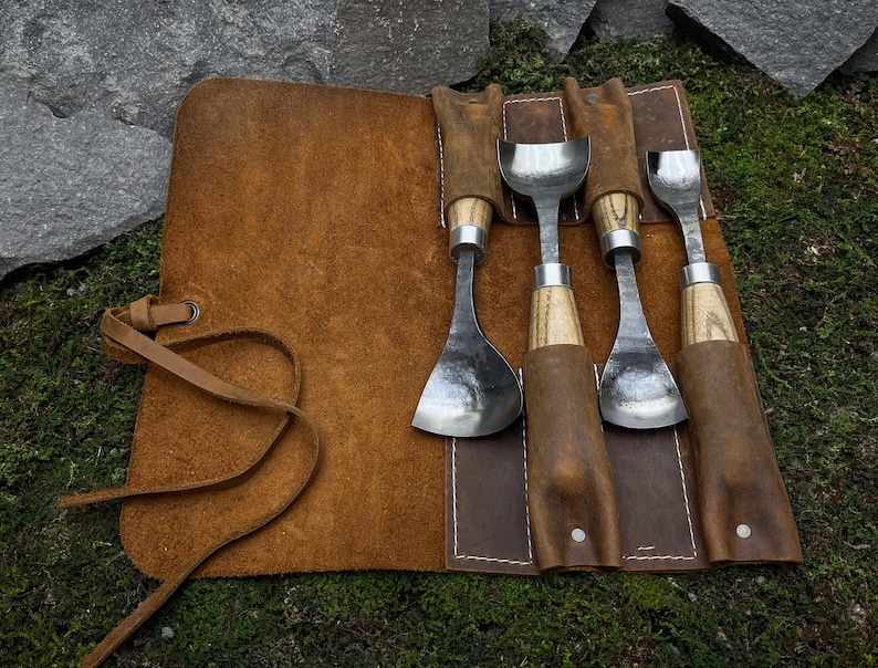 May include: A set of five wood carving tools with leather handles, rolled up in a brown leather carrying case with a strap.