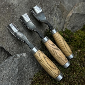 May include: Three wood carving tools with wooden handles. The tools have a curved blade and a metal ferrule. The handles are made of light brown wood with dark brown streaks.