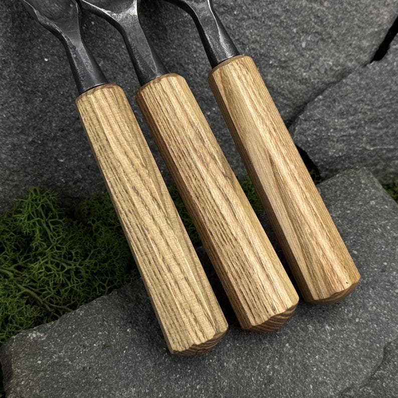May include: Three hand tools featuring light brown, straight-grained wooden handles with a hexagonal profile. The handles are attached to dark, forged metal shafts that extend upward. The tools are arranged side-by-side in a parallel formation.