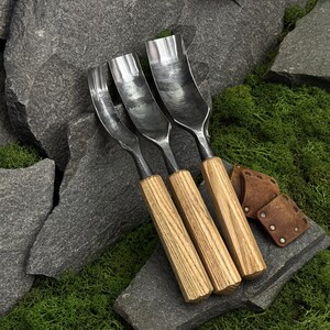 May include: Three wood carving gouges with curved metal blades and light-colored wooden handles. The tools feature varying blade widths and are arranged side by side. Two small, square, brown leather protective covers with metal rivets are included.