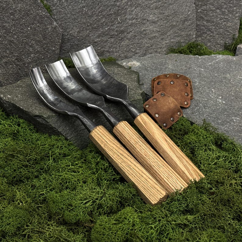 May include: Three wood carving gouges with curved metal blades and light brown wooden handles. The tools feature polished steel heads with varying widths and are accompanied by two small, square brown leather blade guards with metal rivets.