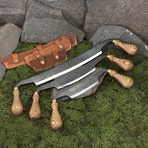 May include: Three curved blade knives with wooden handles and a brown leather sheath. The blades are dark metal, and the handles have a wood grain pattern. The sheath has multiple compartments and button closures.