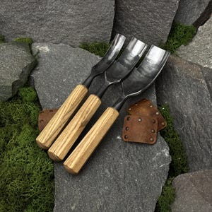 May include: Three metal gouges with curved, polished steel blades and light-colored wooden handles. The tools are arranged side-by-side, accompanied by two small, rectangular brown leather patches secured with metal rivets.