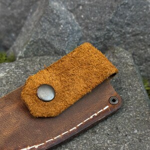 Close-up of Crazy Horse leather knife sheath strap with metal snap button and natural leather texture