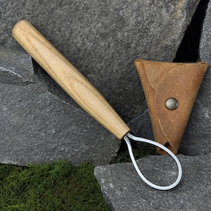 May include: A pottery loop tool with a light wood handle and a metal loop, next to a brown leather pouch with a snap closure. The tool is designed for shaping and trimming clay.