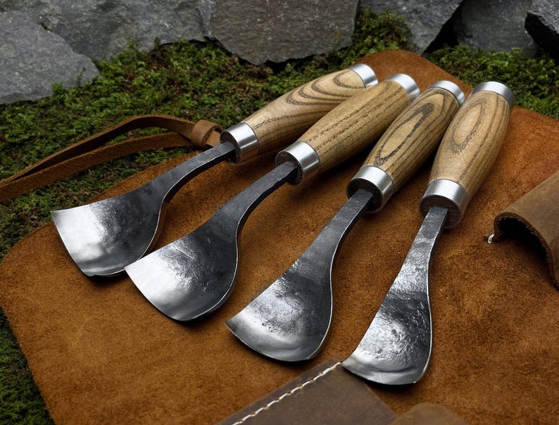 May include: Set of four wood carving tools with curved blades and wooden handles. The tools are laid out on a brown leather surface.