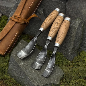 May include: Three wood carving gouges with curved metal blades and light brown wooden handles. Each tool features a silver metal ferrule connecting the blade to the handle. The gouges are arranged side by side, showcasing their distinct curved shapes.
