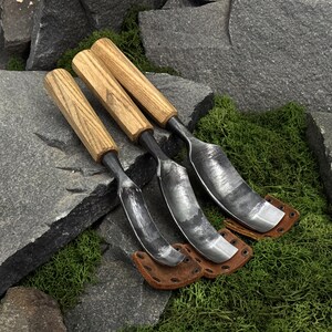 May include: Three hand tools with light brown wooden handles and curved, dark grey metal blades. Each tool features a distinct metal shape and is paired with a small, brown leather protective cover secured with metal rivets at the base.