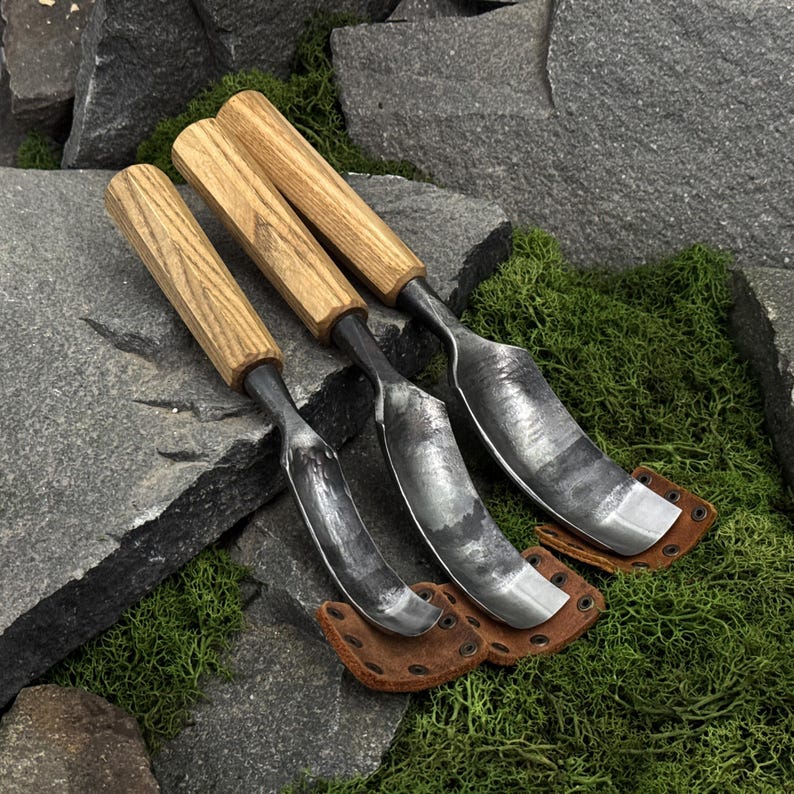 May include: Three hand tools with light brown wooden handles and curved, dark grey metal blades. Each tool features a distinct metal shape and is paired with a small, brown leather protective cover secured with metal rivets at the base.