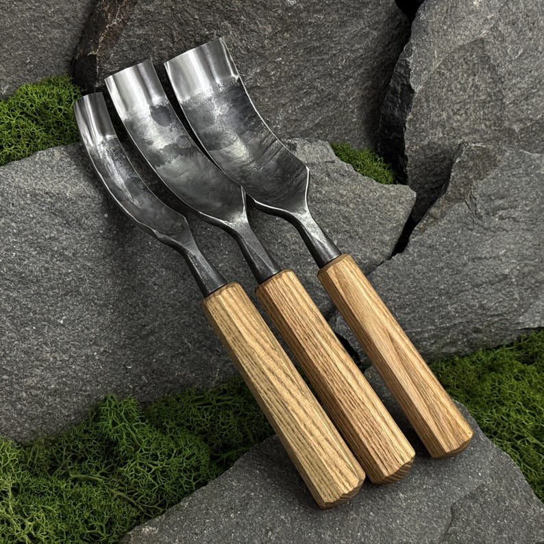 May include: Three metal gouges with curved, polished steel blades and light brown wooden handles. Each tool features a distinct width, showcasing a metallic finish with visible texture on the steel, arranged side by side in a linear formation.