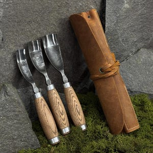 May include: A set of three metal wood carving gouges with curved blades and light brown wooden handles, accompanied by a tan leather roll-up tool case featuring a leather tie closure and a metal grommet detail for secure storage and organization.