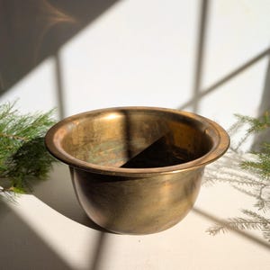 Peut inclure: Un bol en laiton vintage avec un large bord et un corps arrondi. Le bol a une teinte dorée chaude avec de subtiles variations de couleur. L'intérieur est sombre et l'extérieur montre des signes d'âge. Une pièce décorative.