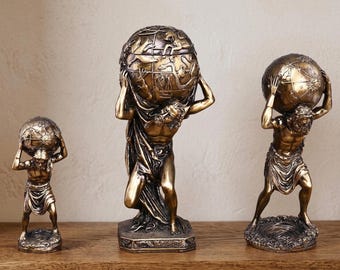 May include: Three bronze-colored statues of Atlas holding globes. The statues vary in size and detail, with the largest one in the center. The figures are muscular and draped in cloth, with the globes intricately detailed.