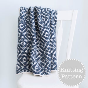 Puede incluir: Una manta de punto azul y blanco con un patrón geométrico, drapeada sobre una silla blanca. La manta está doblada por la mitad y los bordes son visibles. El texto "Knitting Pattern" está impreso en un círculo gris en la esquina inferior derecha de la imagen.