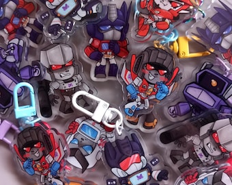 Puede incluir: Una colección de llaveros de personajes de dibujos animados de colores. Los llaveros presentan varios robots en rojo, azul, morado y gris. Algunos llaveros tienen cierres y bucles metálicos para sujetarlos a llaves o bolsos.