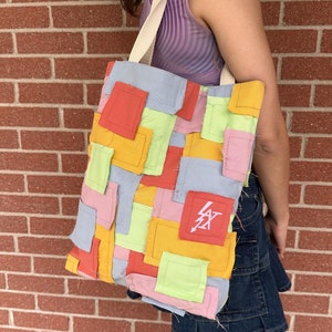May include: A patchwork tote bag featuring a variety of colours, including red, orange, yellow, green, blue, and pink. The bag has a large, white "LAX" logo on the front.