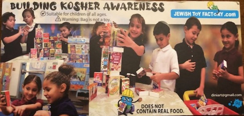 以下が含まれることがあります： 子供たちが、おもちゃの食料品店セットで遊んでいます。セットには、シリアル箱、ジュースボックス、スープ缶など、さまざまな模擬食品が含まれています。子供たちは塔を建てて、お店屋さんごっこをしています。画像には、「Building Kosher Awareness」と「Jewish Toy Factory.com」のテキストが含まれています。