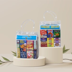 以下が含まれることがあります： 2つの透明なプラスチック製のバッグに、ミニチュアの箱に入ったコーシャースナックが入っています。バッグには持ち手があり、薄いベージュの表面に置かれています。スナックには、プレッツェル、アップルジュース、スプリンクルクッキー、ハニーグラハムクラッカー、ティービスケット、ヨーグルトなどがあります。